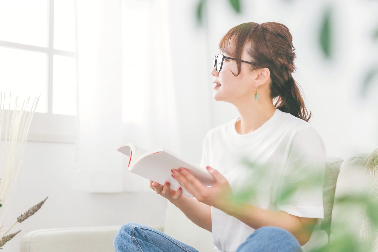 本を読んでいる手を止めて、窓の外を見る女性の写真画像です。