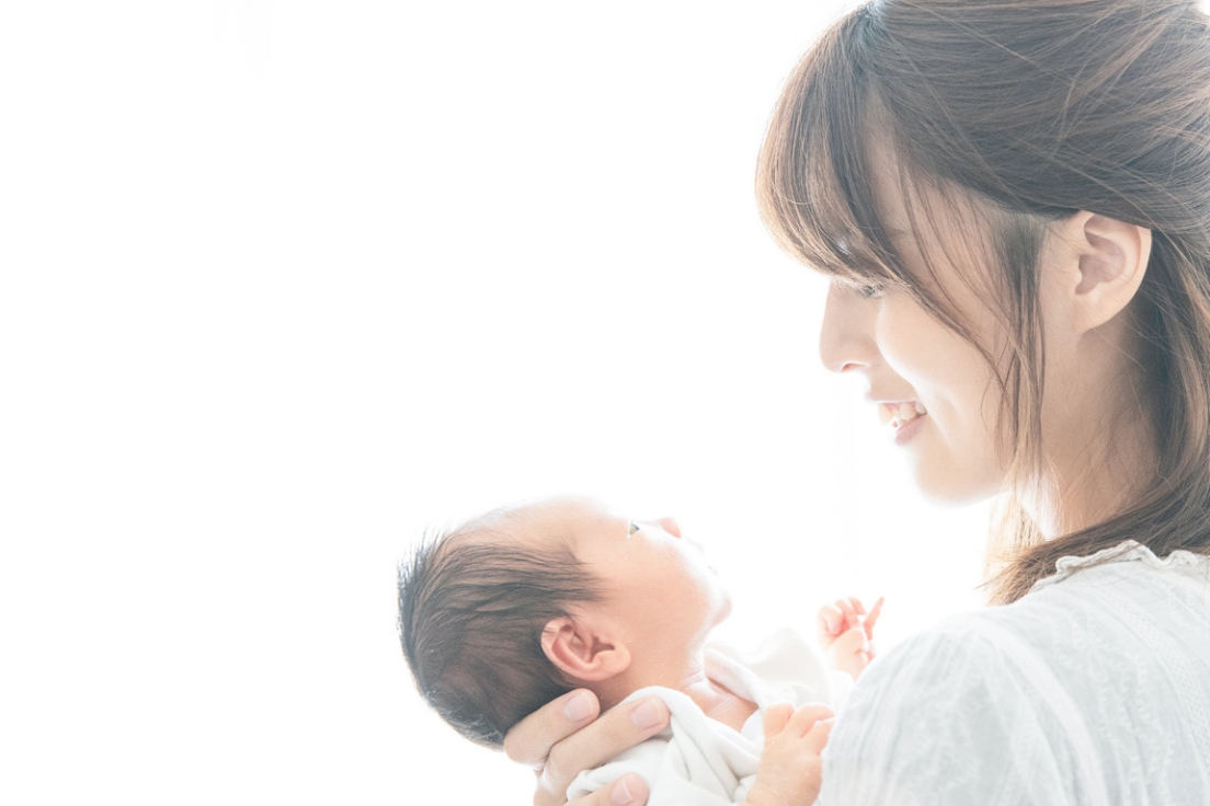 生まれたばかりの赤ちゃんを抱っこして笑顔で微笑みかけるママの写真画像です。