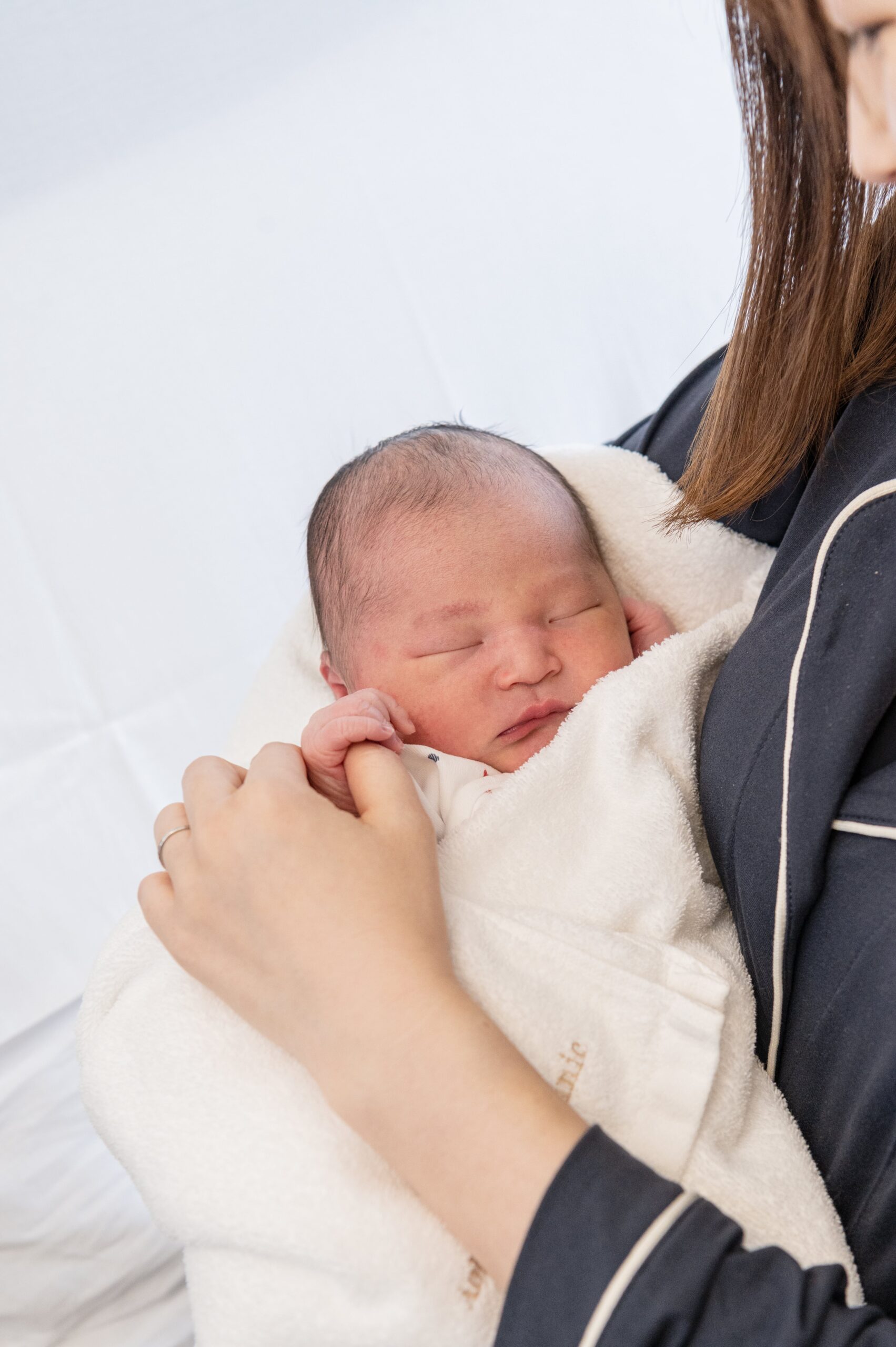 すやすや眠る赤ちゃんを優しく抱っこするママの写真です。ママの親指を赤ちゃんがぎゅっと握っています。